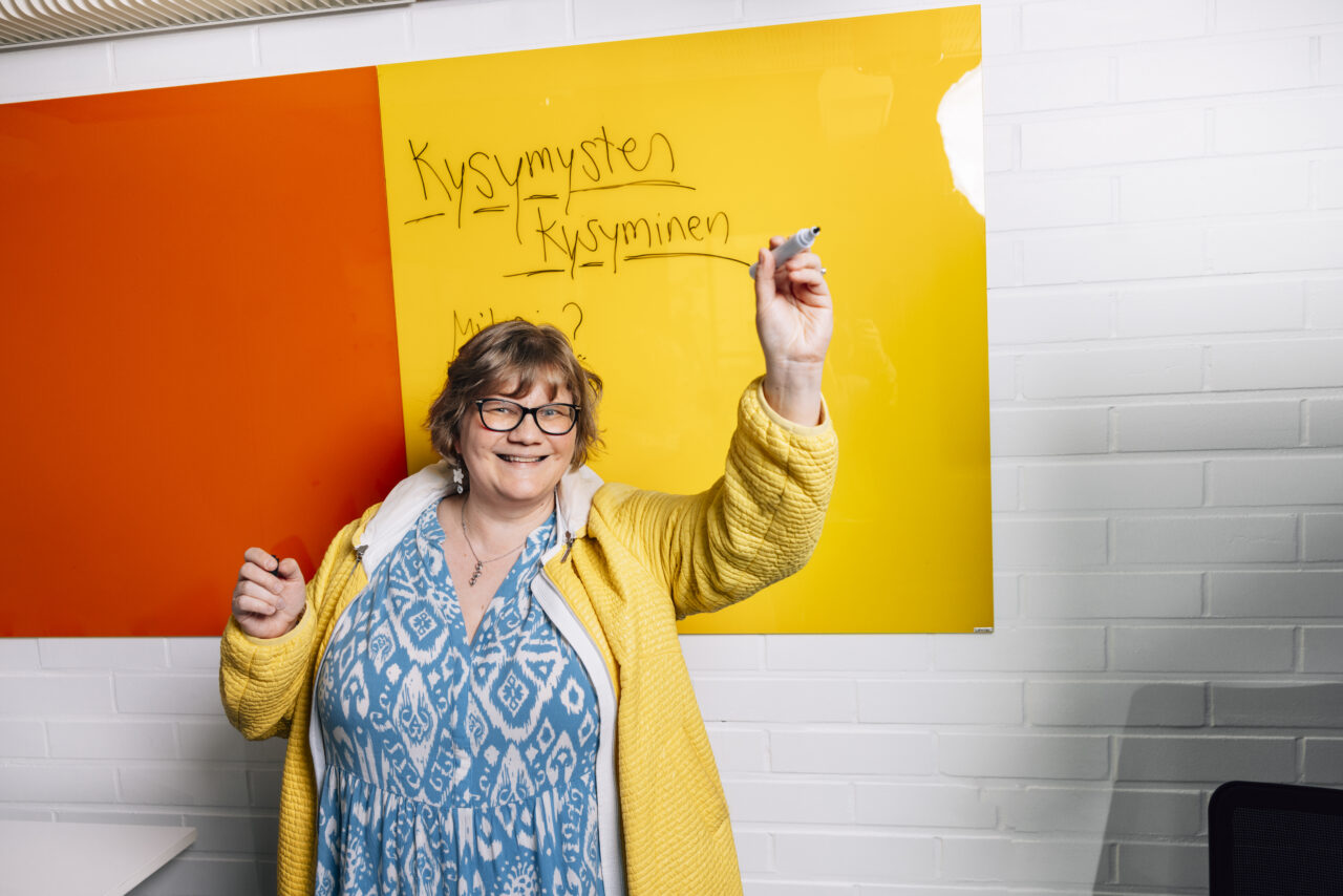 Kouluttaja innostuu taulun edessä, jossa lukee "Kysymysten kysyminen"