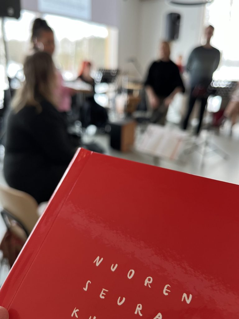 NSV-kirja ja taustalla musisoijia