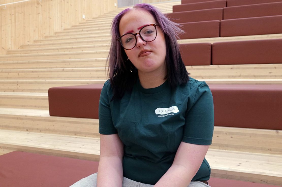 Nuori istuu portailla ja hymyillen katsoo kohti kameraa