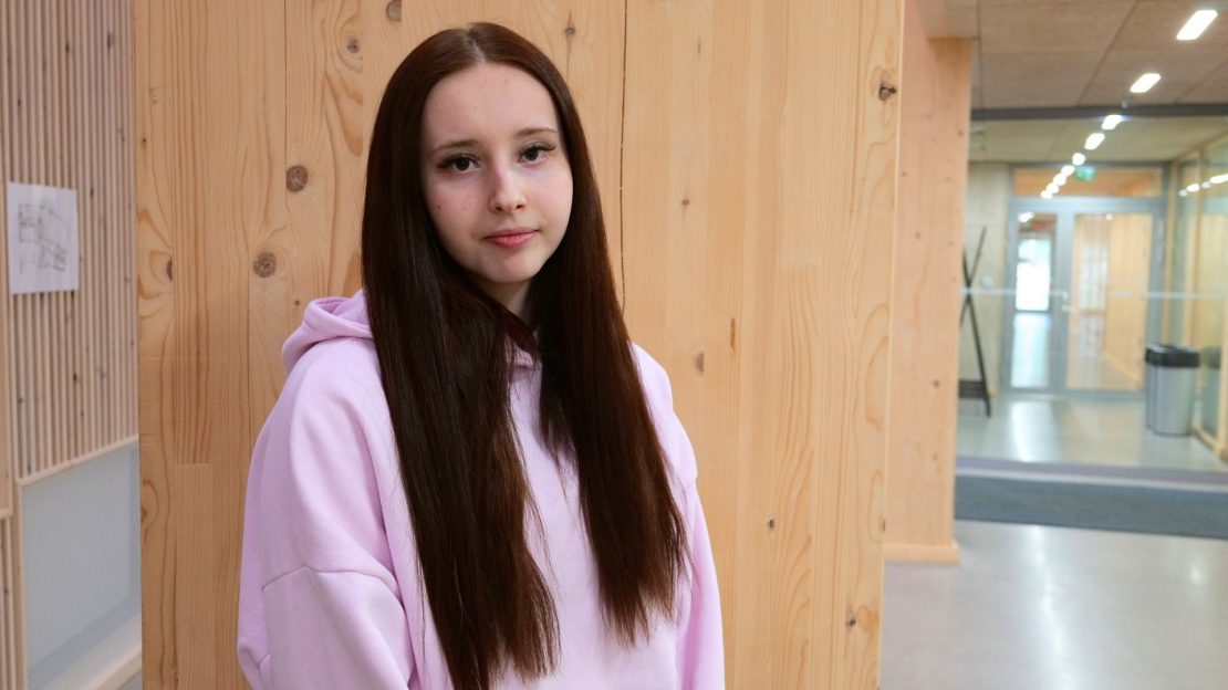 Opiskelija seisoo seinän edustalla päällään vaaleanpunainen huppari.